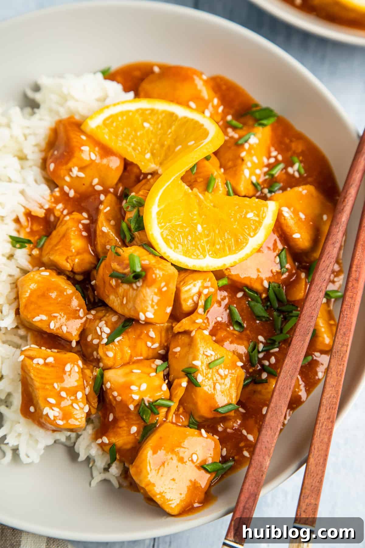 Overhead shot of Instant Pot orange chicken on a plate, garnished with an orange twist and fresh herbs.
