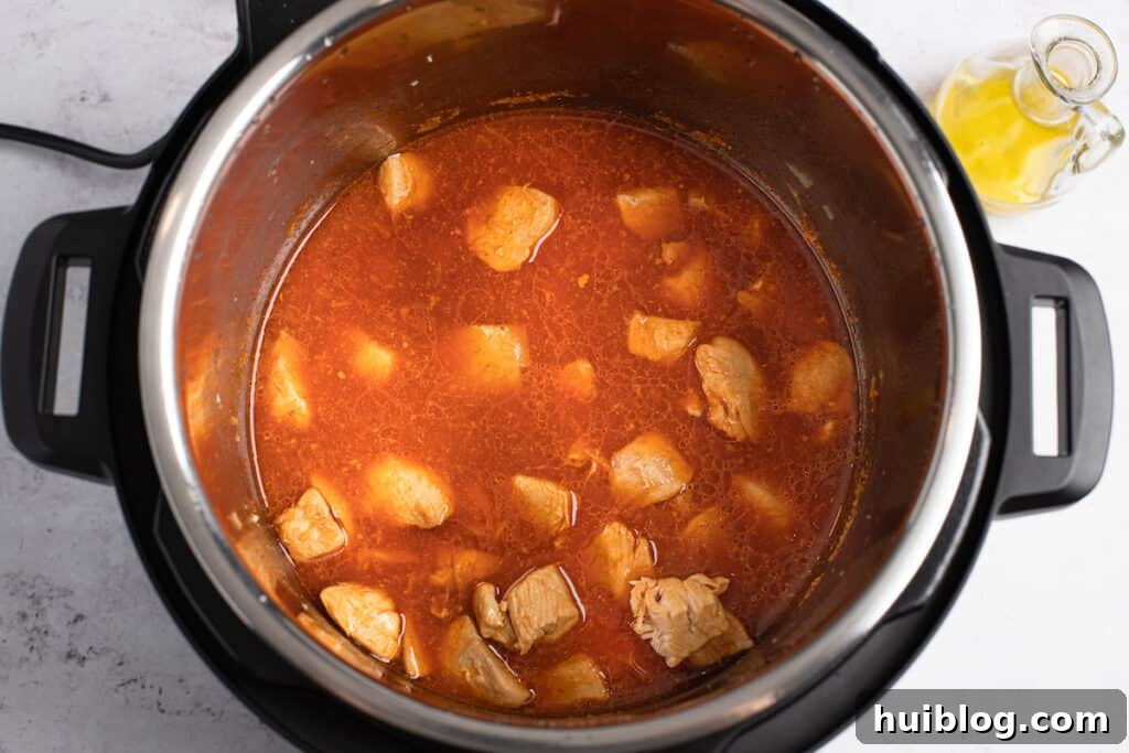 Cooked chicken pieces submerged in the simmering orange sauce within the Instant Pot.