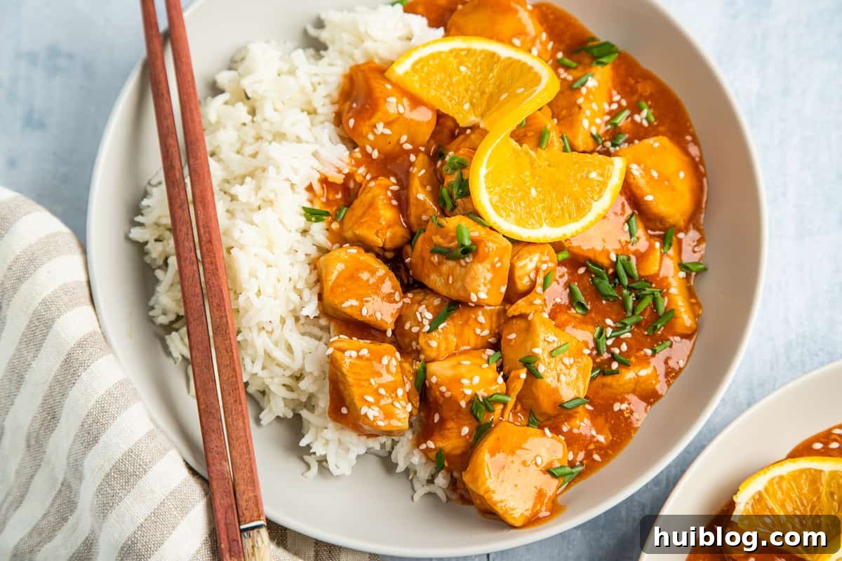 A beautifully plated serving of Instant Pot orange chicken, accompanied by white rice and garnished with orange wedges and chopsticks.