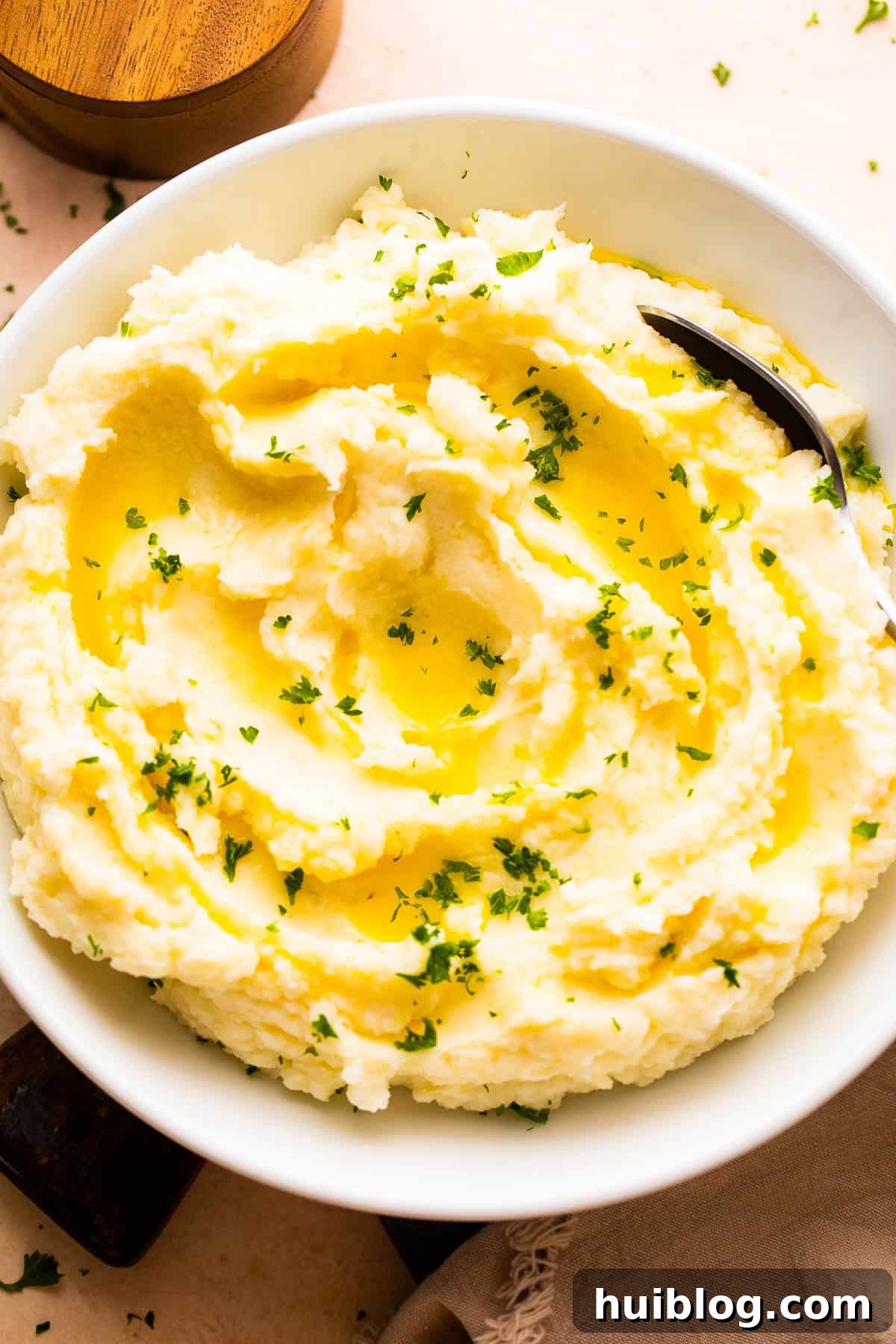 overhead shot of a bowl with creamy mashed potatoes garnished with melted butter and parsley