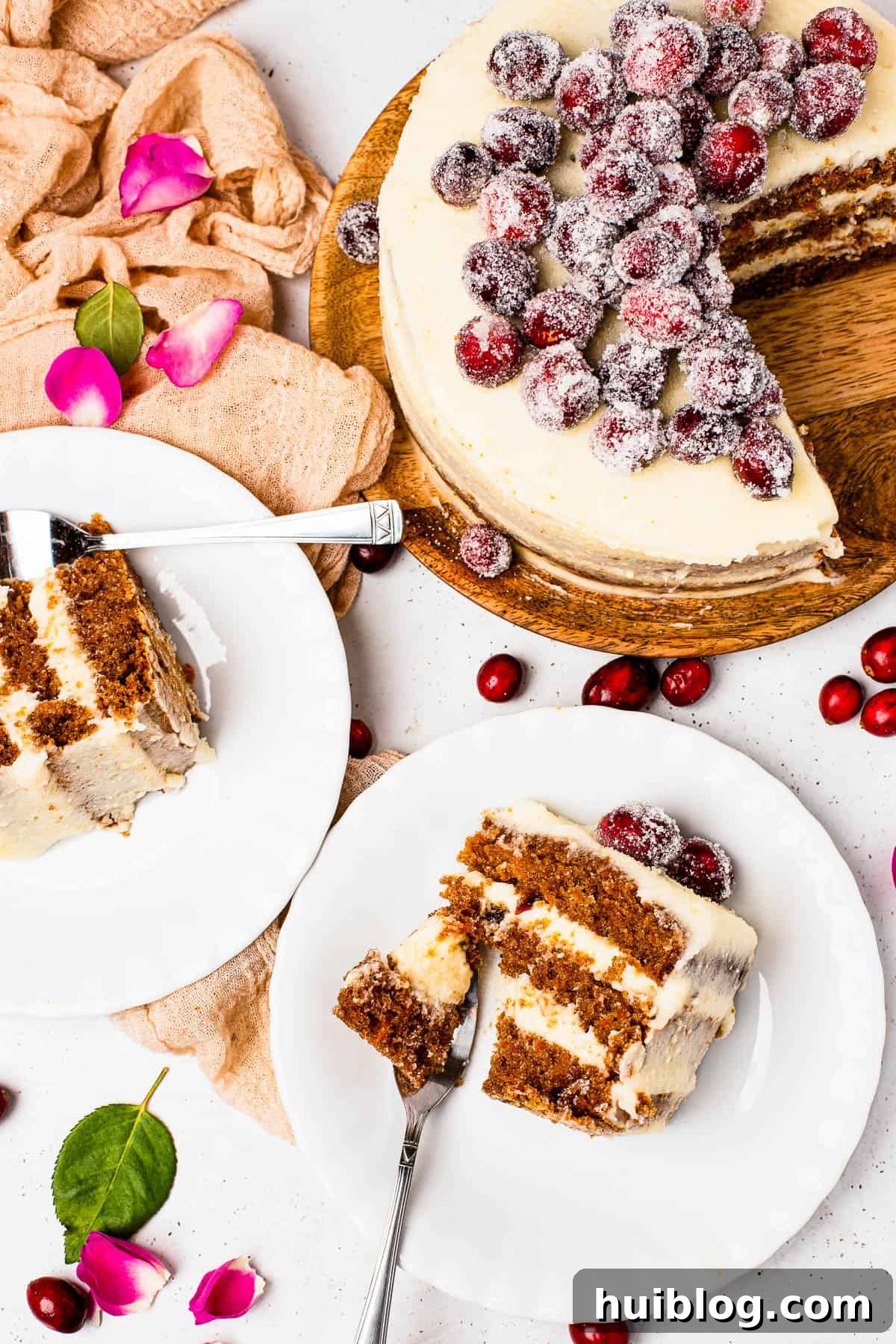 Slices of sugared cranberry layer cake on dessert plates, next to the remaining cake on a cake stand, decorated with fresh rosemary and sugared cranberries.
