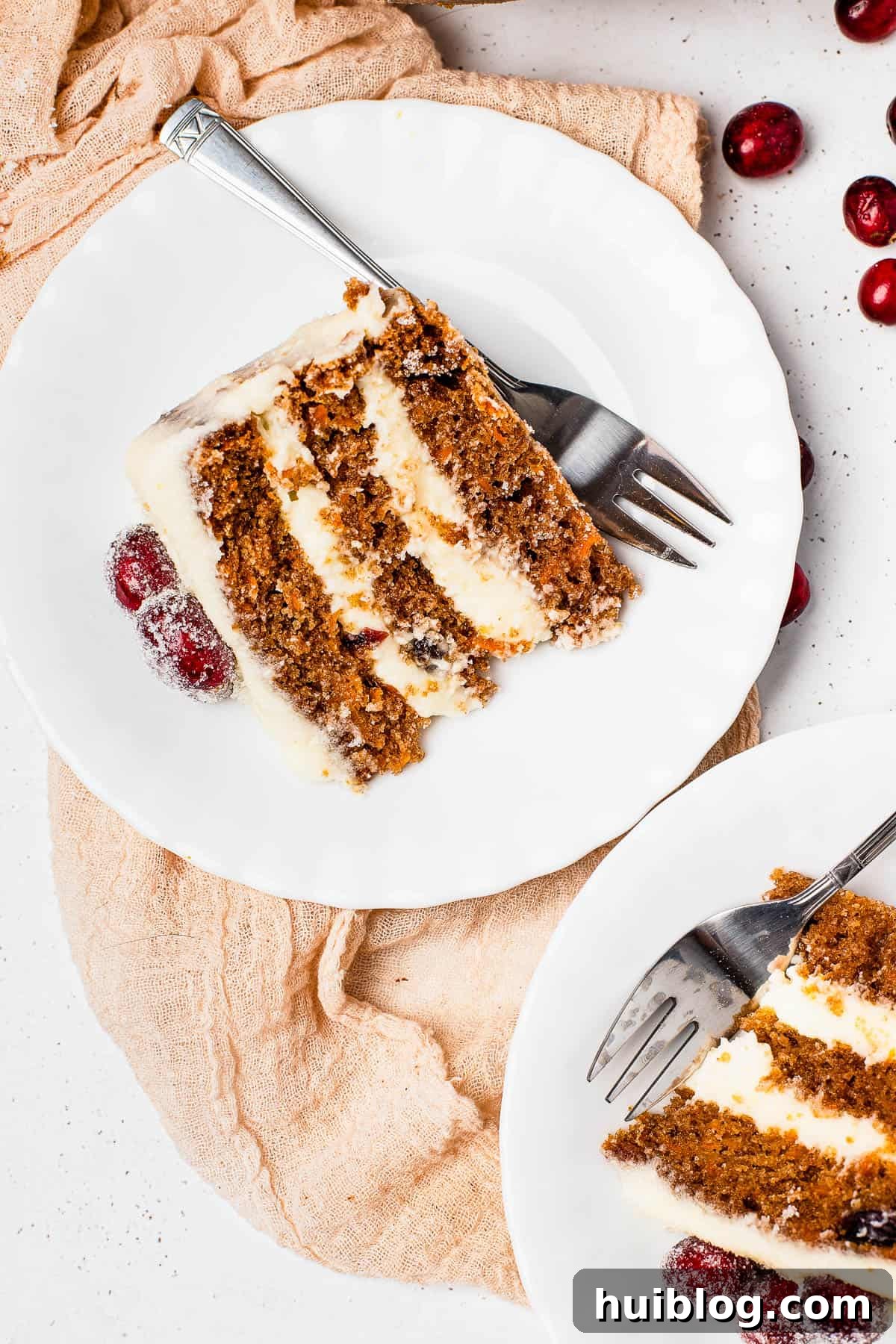 A close-up shot of a slice of cranberry carrot layer cake on a dessert plate with a fork, showing the moist layers and cranberries.