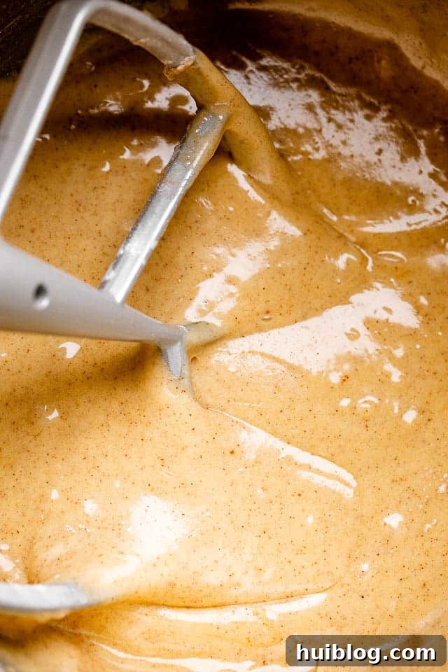 Mixing the rich, spiced carrot cake batter to perfection. Close-up shot of a hand mixing a vibrant orange carrot cake batter in a large mixing bowl with an electric mixer.
