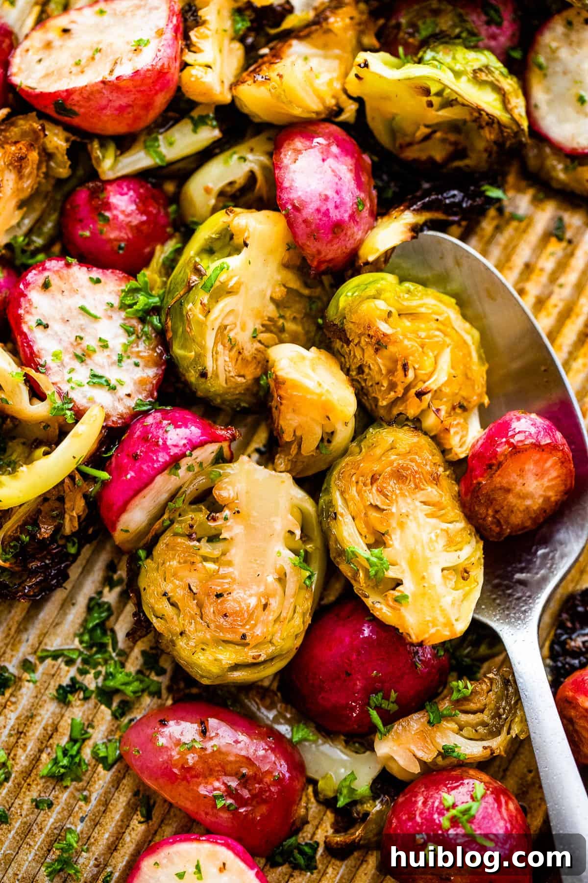 Halved Brussels sprouts and radishes spread evenly on a parchment-lined baking sheet, glistening with olive oil, ready for roasting.