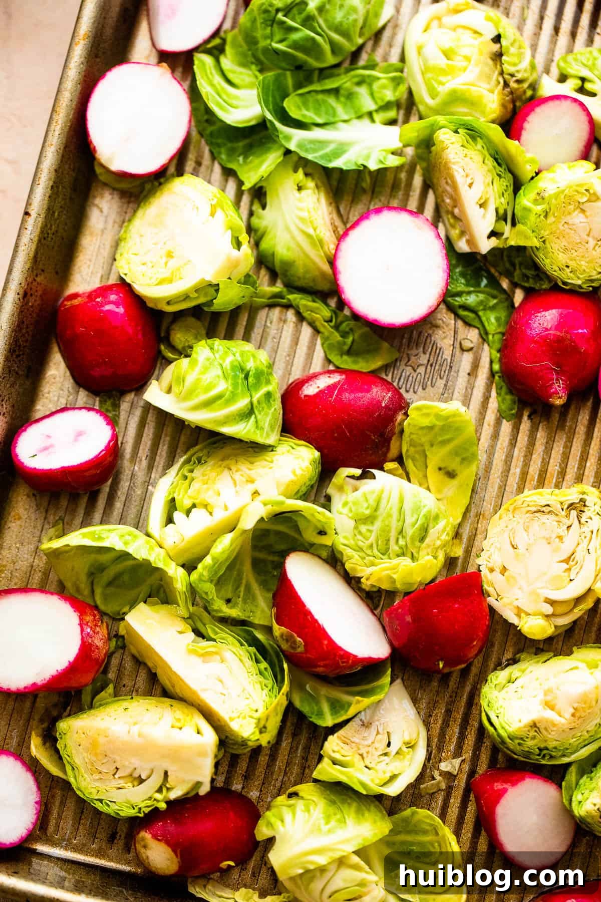 A mix of fresh, halved Brussels sprouts and radishes in a large mixing bowl, coated with olive oil, salt, and pepper.
