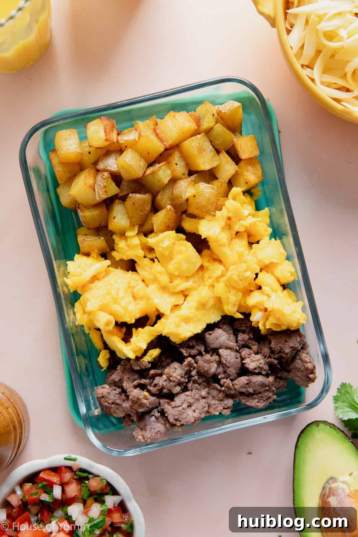 Meal prep breakfast bowls showing potatoes, eggs, and sausage in a to go glass container.