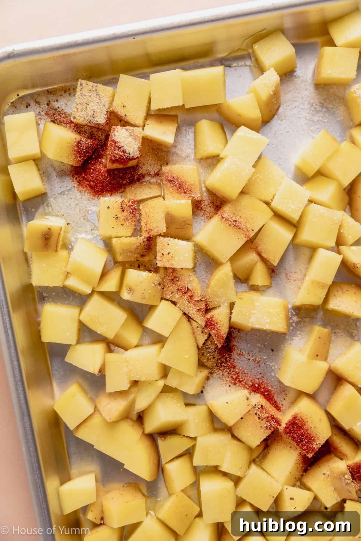 Cubed potatoes on a baking sheet drizzled with oil and sprinkled with seasonings.