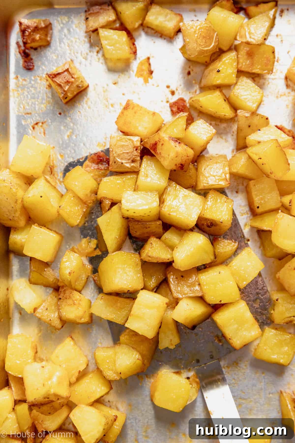 Roasted potatoes on a baking sheet being scooped by a spatula.