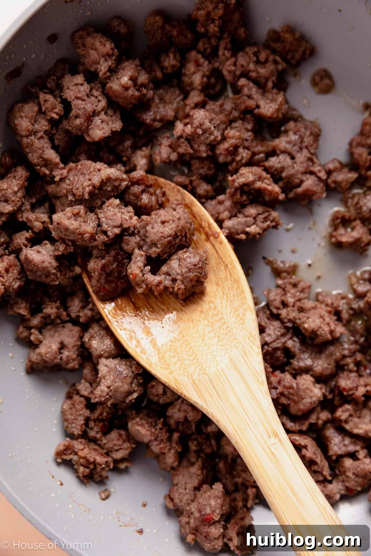 Cooked sausage in a skillet with a wooden spoon.