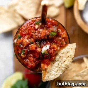 Overhead view of a jar of homemade sals with a tortilla chip being dipped in.