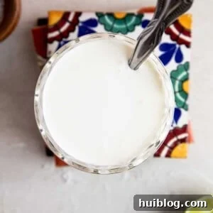 Overhead of a glass filled with mexican cream sauce with a spoon dipping in.