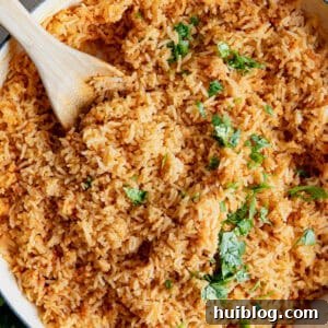 Restaurant style Mexican Rice in a skillet being served with wooden spoon.