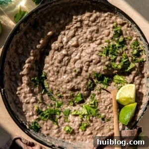 Skillet filled with refried beans, topped with cilantro and lime wedges.