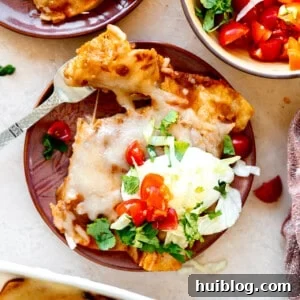 Plate of cheese enchiladas with Tex Mex chili gravy ad topped with sour Cream, shredded lettuce, diced tomatoes and fresh cilantro.