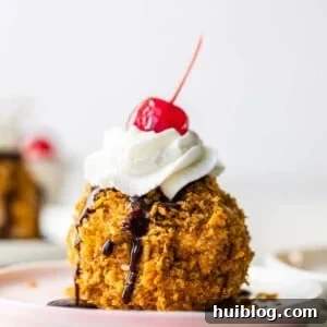 Easy to make mexican fried ice cream on a pink plate topped with drizzles of chocolate fudge, whipped cream and a cherry on top.