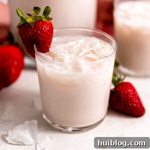 Small glass filled with light pink, strawberry horchata, with a strawberry on the rim of the glass as a garnish.