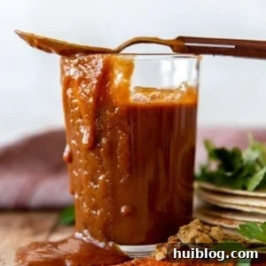 Cup filled with homemade enchilada sauce, with sauce dripping down the side and a spoon on top.