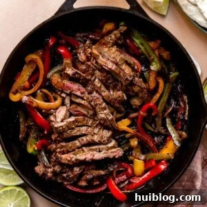 Large cast iron skillet filled with sliced grilled steak and grilled bell peppers and onions.